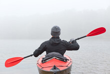 Back View Image Of Young Man Kayaking On Lake Or Rover In Boat, Using Red And Black Oar, Wearing Gray Cap And Black Jacket, Spending Early Morning Doing Water Sport.