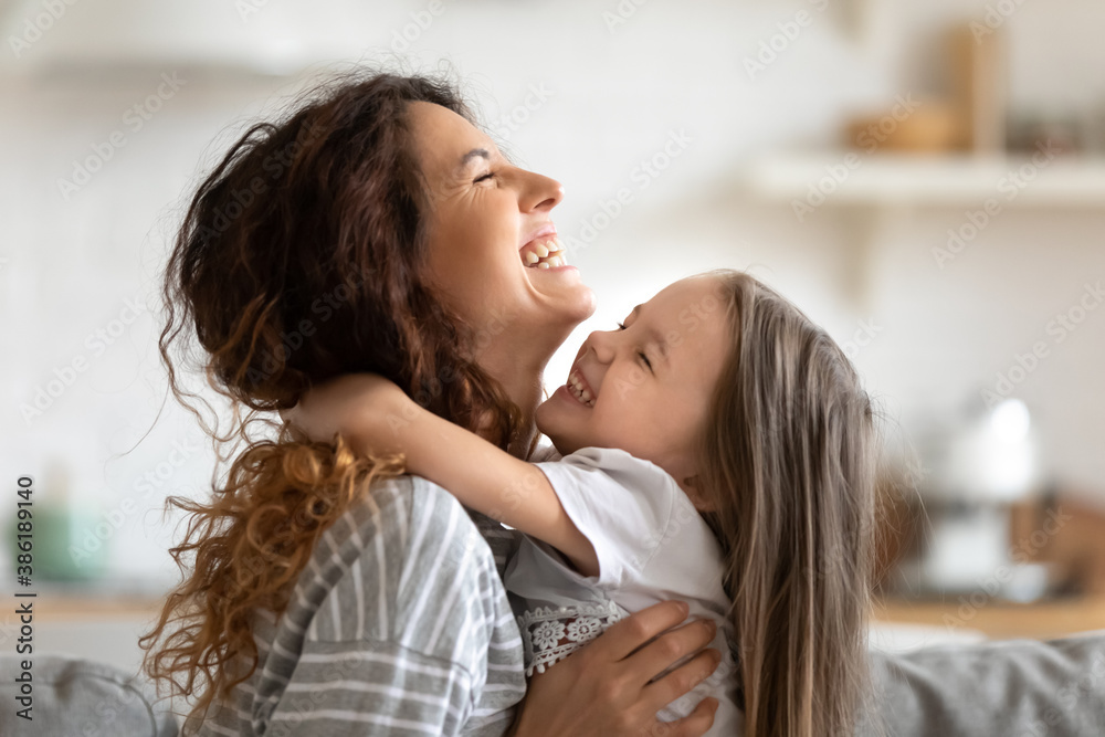 Close up side view overjoyed smiling young mother and daughter hugging and laughing, enjoying tender moment, happy mum and adorable preschool girl kid cuddling, having fun together at home - obrazy, fototapety, plakaty 