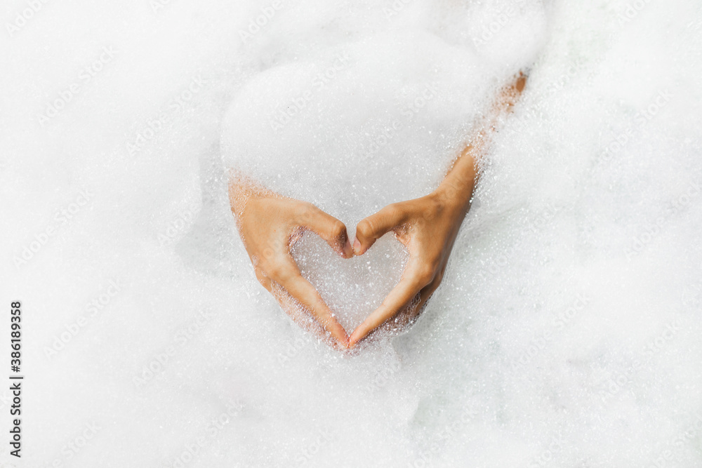 Woman hands in heart shape in bath full of foam bubbles close-up. Spa beauty treatment. Love symbol - obrazy, fototapety, plakaty 