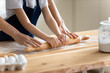 Close up caring mother and little daughter wearing aprons rolling out dough together, working with rolling pin, standing at wooden countertop in kitchen, family cooking baking together