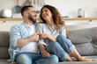 © fizkes - Happy married young couple hugging, sitting on cozy couch together, overjoyed laughing woman and man having fun, enjoying leisure time, relaxing on sofa in living room at home, good relationship
