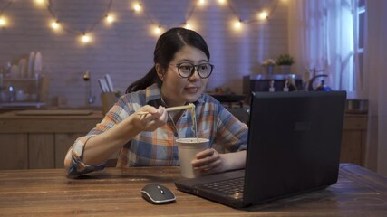 Wall Mural - Pretty asian korean woman eating ramen soup and watching series on laptop computer in home kitchen late at night.