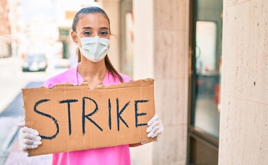 Wall Mural - Young doctor woman wearing medical mask and holding strike banner cardboard at street of city.