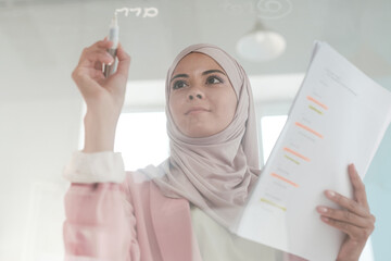 Poster - Young serious female broker in hijab holding financial papers and highlighter