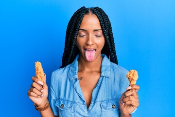 Beautiful hispanic woman eating chicken wings sticking tongue out happy with funny expression.