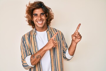 Young hispanic man wearing casual clothes smiling and looking at the camera pointing with two hands and fingers to the side.