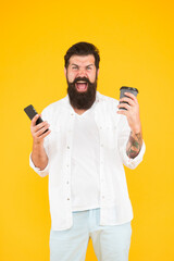 real winner. use modern technology. happy bearded man holding phone while drink coffee. brutal hipster drinking takeaway beverage. angry guy with beard and moustache has mobile phone. morning routine