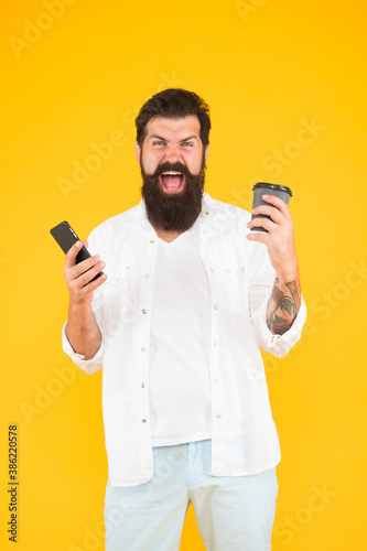 real winner. use modern technology. happy bearded man holding phone while drink coffee. brutal hipster drinking takeaway beverage. angry guy with beard and moustache has mobile phone. morning routine