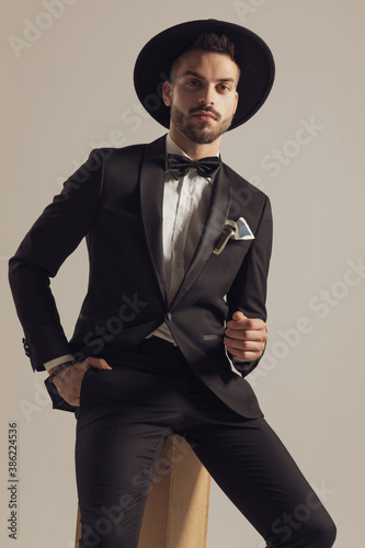 Confident groom holding hand in pocket, wearing hat and tuxedo