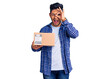 © Krakenimages.com - Handsome latin american young man holding delivery package smiling happy doing ok sign with hand on eye looking through fingers