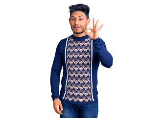 Handsome latin american young man wearing casual winter sweater smiling positive doing ok sign with hand and fingers. successful expression.