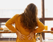 Back view of faceless young woman touching back feeling backache, discomfort low lumbar muscular kidney pain sitting with pain