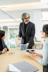 Sticker - Confident mature broker with touchpad looking at one of female colleagues