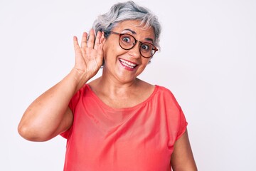 Wall Mural - Senior hispanic grey- haired woman wearing casual clothes and glasses smiling with hand over ear listening an hearing to rumor or gossip. deafness concept.