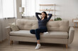© fizkes - Happy millennial Vietnamese girl sit relax on sofa in living room look in window distance dreaming thinking. Smiling young asian woman renter rest on couch at home visualize imagine on weekend.