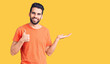 © Krakenimages.com - Young handsome man with beard wearing casual t-shirt showing palm hand and doing ok gesture with thumbs up, smiling happy and cheerful