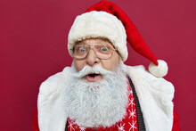 Surprised Excited Funny Old Bearded Santa Claus Face Wearing Glasses Costume Looking At Camera, Surprised Advertising Christmas Promotion, Xmas Discount Ad Isolated On Red Background, Haedshot.