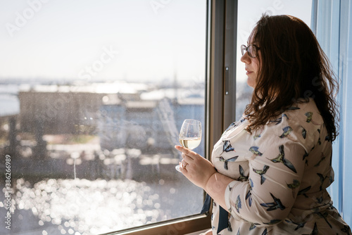 Fotomural A large woman stands at the window with a glass of wine