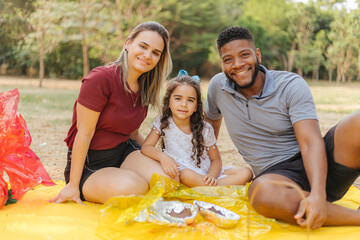 Wall Mural - happy latin family celebrating Easter. curly girl holding a chocolate egg in the park