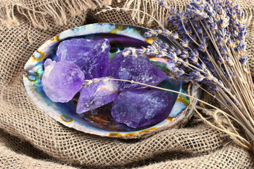 Wall Mural - A close up image of several rough pieces of amethyst crystal in an abalone shell with dried lavender flowers. 