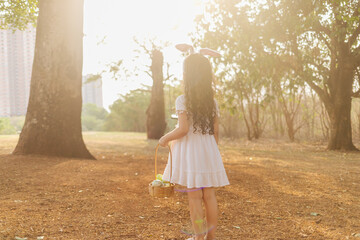 Wall Mural - latin girl wearing bunny ears and holding a hamper of easter eggs in the park