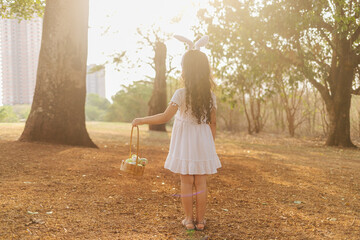 Wall Mural - latin girl wearing bunny ears and holding a hamper of easter eggs in the park