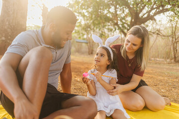 Wall Mural - Latin family celebrating Easter. curly girl wearing bunny ears and painting an easter egg