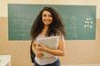Leinwandbild Motiv Latin Curly haired student smiling wearing backpack holding a notebook in a classroom