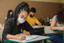 Latin Students In The Classroom. Female Student With Twisted Hair Wearing Mask And Writing In Notebook With A Pen. Covid-19. Pandemic.