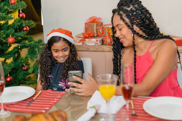 Wall Mural - Summer Christmas dinner in Brazil. Real Brazilian family having fun at the Latin American Christmas party. sisters looking at the phone. child with curly hair