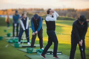 Group of golfers practicing and training golf swing on driving range practice, men playing on golf course, golf ball at golfing complex club resort