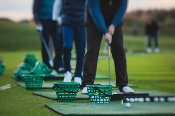 Group of golfers practicing and training golf swing on driving range practice, men playing on golf course, golf ball at golfing complex club resort