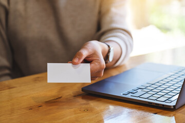 Wall Mural - Closeup image of a woman holding and giving a blank business cards while using laptop computer