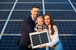 Portrait of a young family holding a small solar panel and a baby boy, smiling and looking at camera. Concept of green generation
