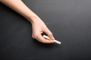 Female hand with piece of chalk on blackboard