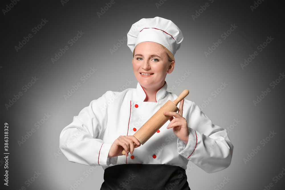 Mature female chef with rolling pin on dark background