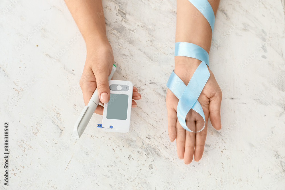 Female hands with awareness ribbon, glucometer and syringe on white background. Diabetes concept