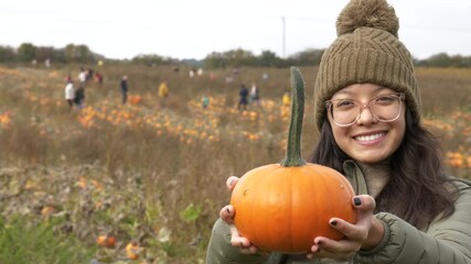 happy woman in warm clothes holding her pumpkin and smiling while at a pumpkin patch