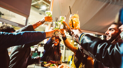 Group of friends drinking at cocktail bar with open face masks - Happy young people having fun together toasting drinks at nightclub - New normal lifestyle concept.