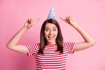 Wall Mural - Photo portrait of cheerful funny girl pointing with fingers on birthday cap smiling isolated on pastel pink color background