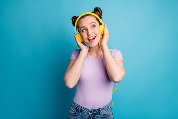 Photo of attractive crazy lady two funny buns good mood listen modern technology earphones sing popular song look up empty space wear casual purple t-shirt isolated blue color background