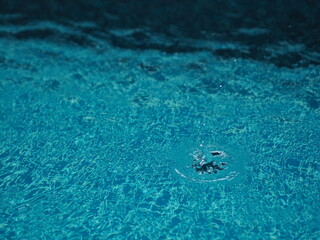 Rain drops falling blue water in pool background ripples on the surface texture, glittering bokeh abstract