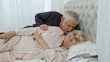 © Andrii Iemelianenko - Senior Caucasian grandparents couple lying in bed at home in morning. Man gently whispering to woman