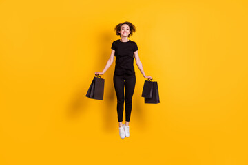 Full length body size view of attractive cheerful funky girl jumping carrying packages bargain store isolated bright yellow color background