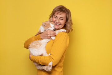 Caucasian woman lovingly hugging cat on yellow wall.