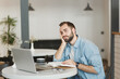 © ViDi Studio - Boring man sitting alone at table in coffee shop cafe working or studying on laptop computer reading book relaxing in restaurant during free time indoors. Freelance mobile office business concept.