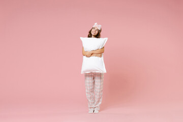 Wall Mural - Full length portrait of smiling pretty young woman in white pajamas home wear sleep mask hold pillow looking up while rest at home isolated on pink background studio portrait. Relax good mood concept.