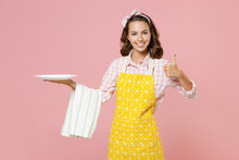 Cheerful Smiling Young Woman Housewife 20s In Yellow Apron Hold Empty Plate Dishcloth Towel Showing Thumb Up Doing Housework Isolated On Pastel Pink Background Studio Portrait. Housekeeping Concept.