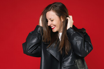 Wall Mural - Smiling pretty charming young brunette woman 20s wearing basic casual black leather jacket white t-shirt keeping eyes closed put hands on head isolated on bright red colour background studio portrait.