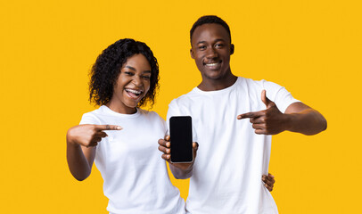 Cheerful black couple showing blank smartphone screen at camera